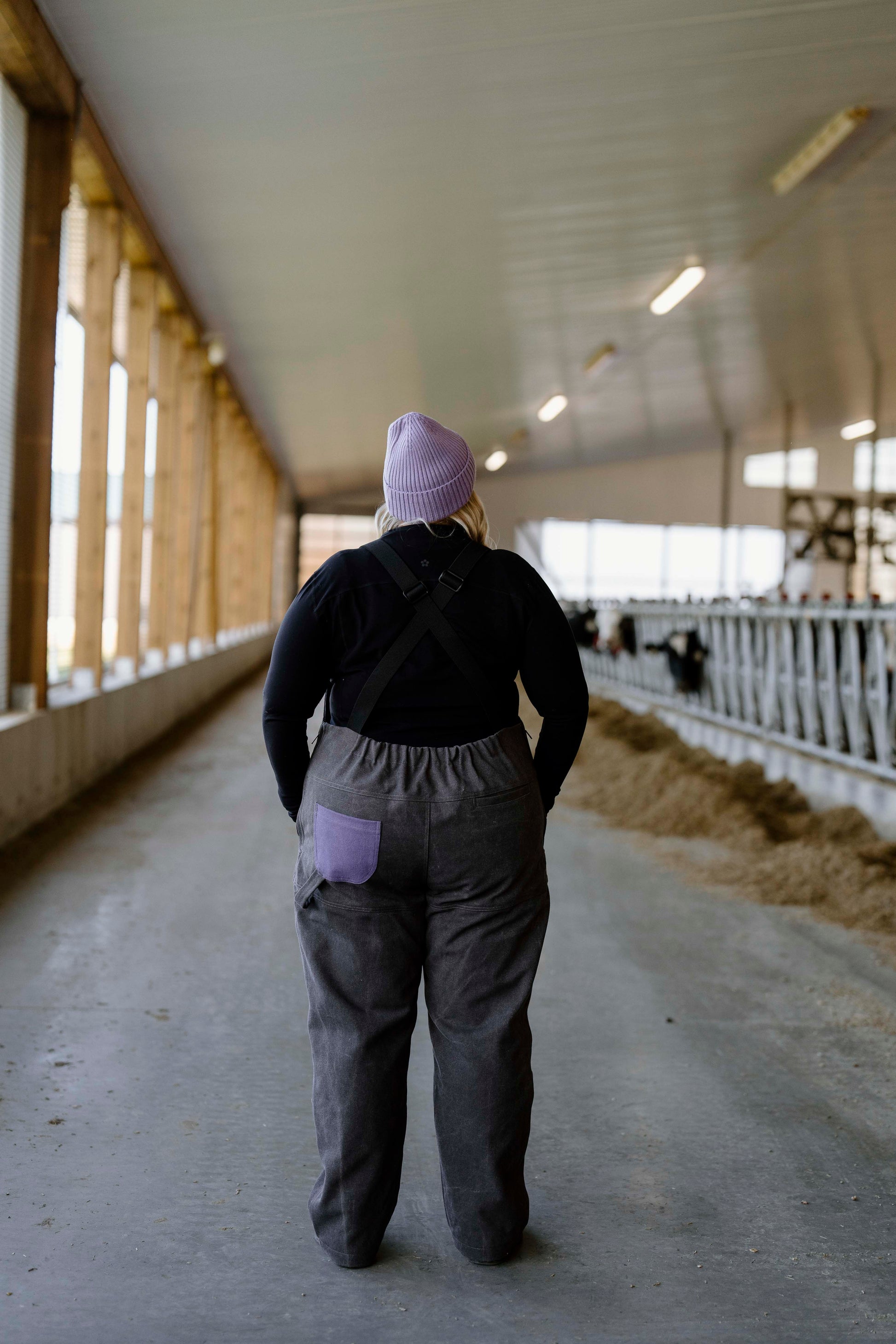 Person wearing grey overalls with purple pocket and toque in barn setting 