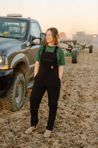 Person wearing black overalls standing next to a truck in a field