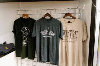 Three t-shirts with different designs hanging on a rack against a white tiled wall.