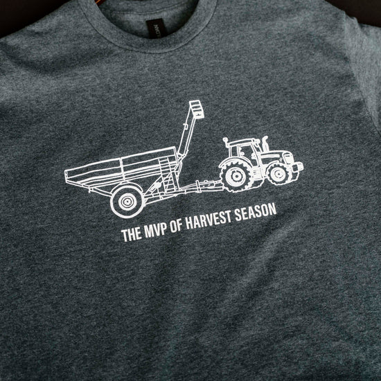 Gray t-shirt with white tractor graphic and text on a hanger against a dark background