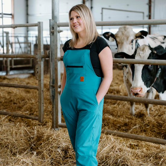 Lady in turquoise overalls standing in cow barn