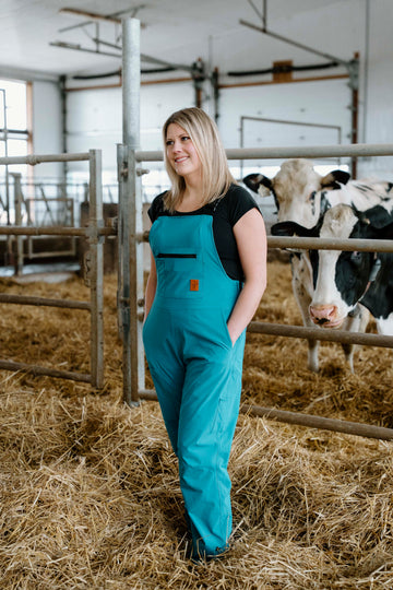 Lady in turquoise overalls standing in cow barn