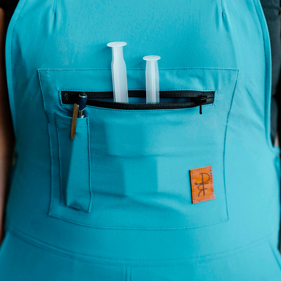 person wearing teal overalls with front bib pocket and pen pocket