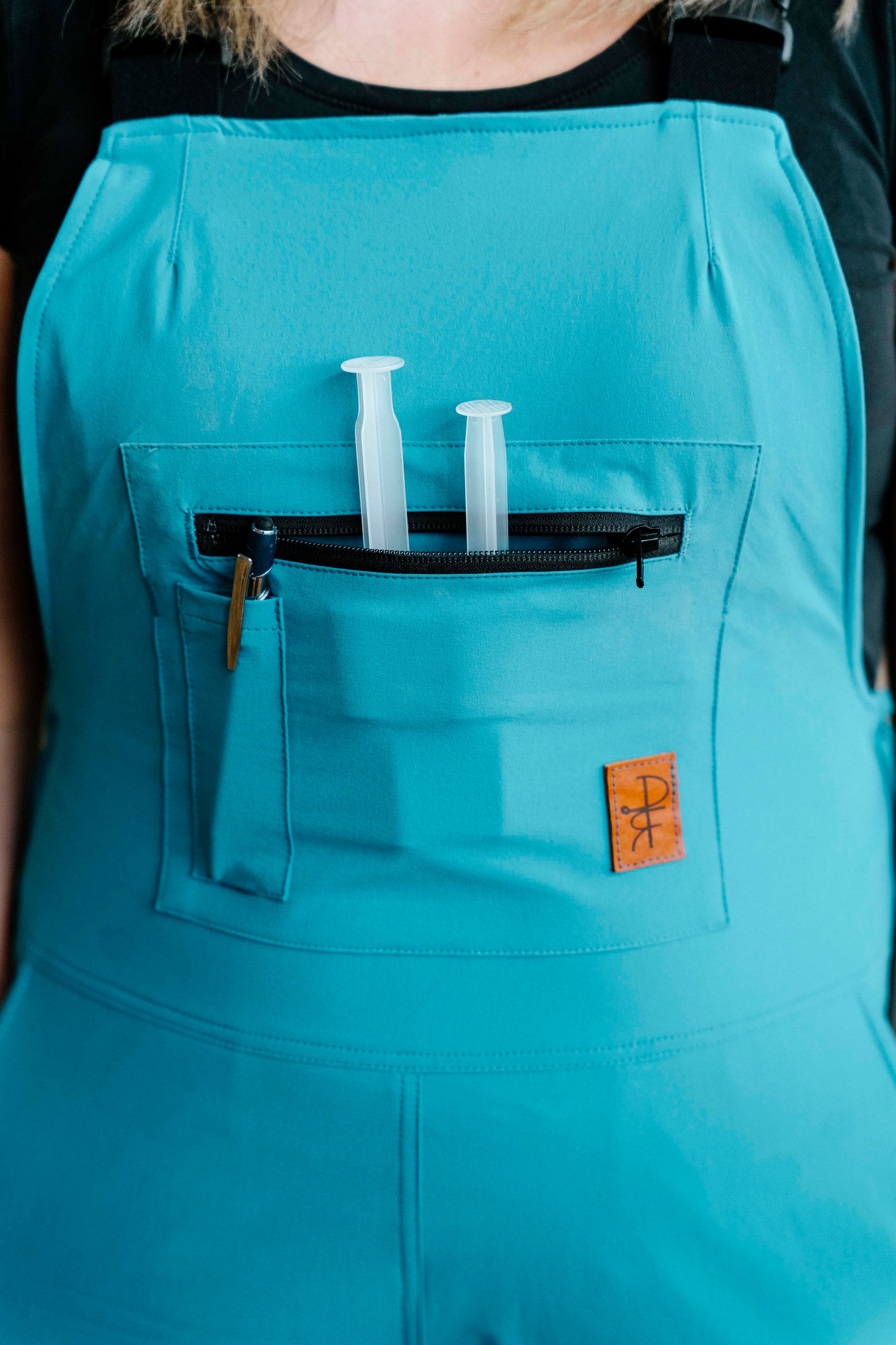 person wearing teal overalls with front bib pocket and pen pocket