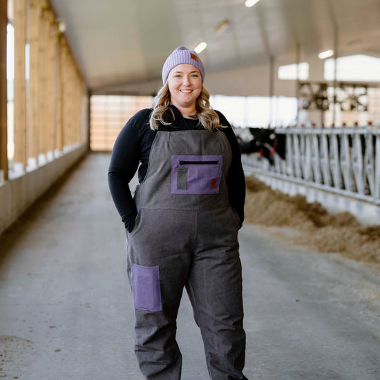 A person wearing a purple and gray insulated overall, standing in a barn setting.