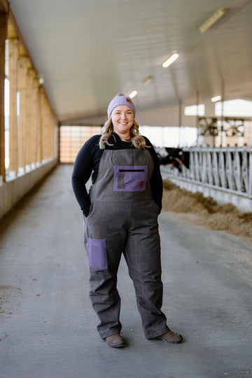 A person wearing a purple and gray insulated overall, standing in a barn setting.
