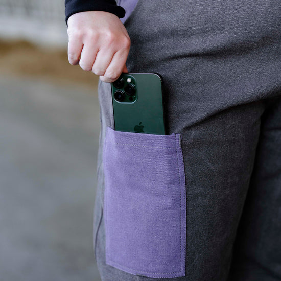 A person wearing lilac insulated overalls with a smartphone in the front pocket.